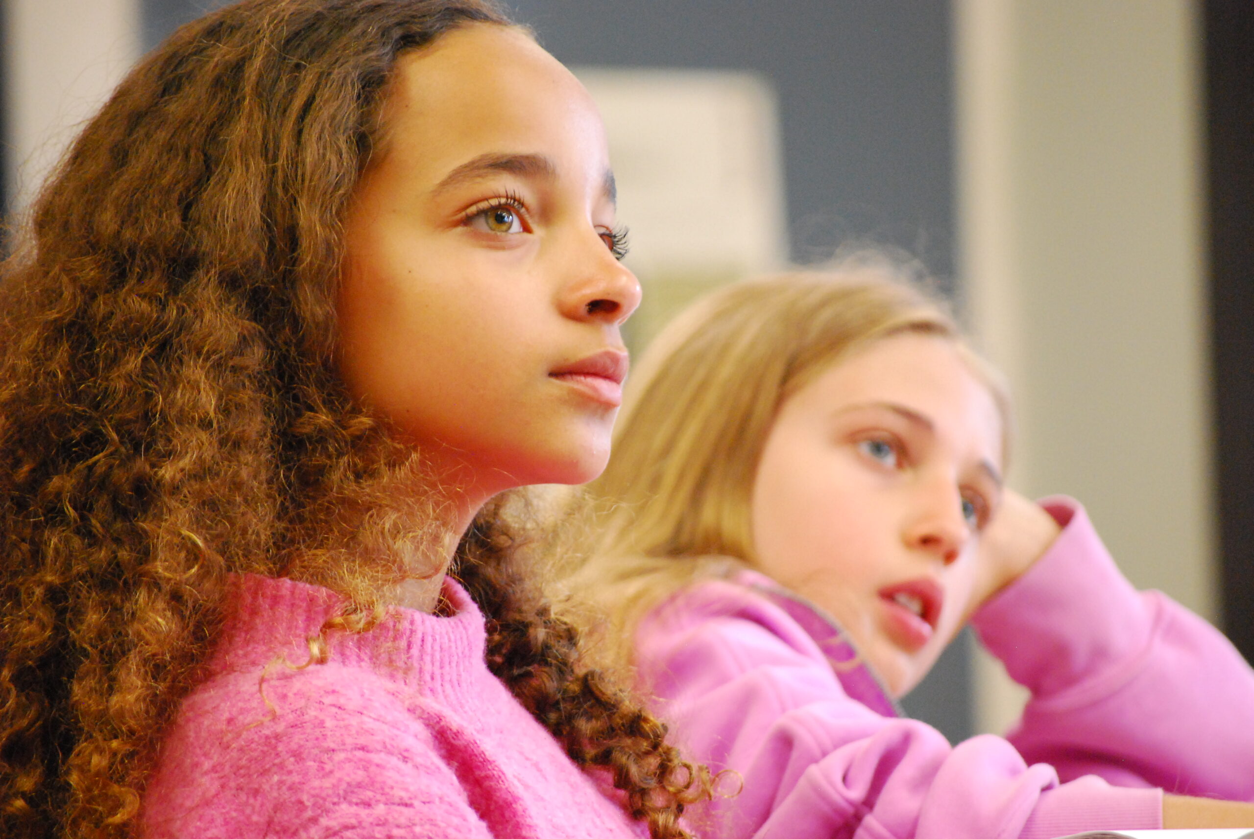 Two girls in a classroom sit at their desks, listening closely to their teacher.