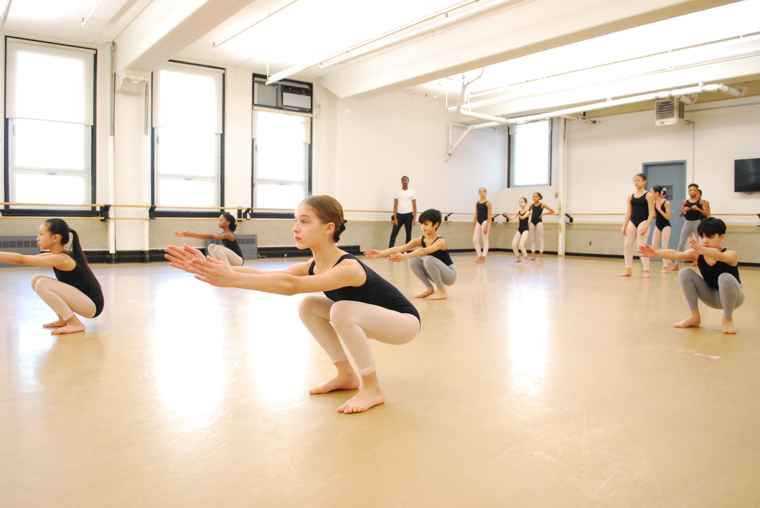 A group of students practice primitive squats of the Horton technique in a dance studio.