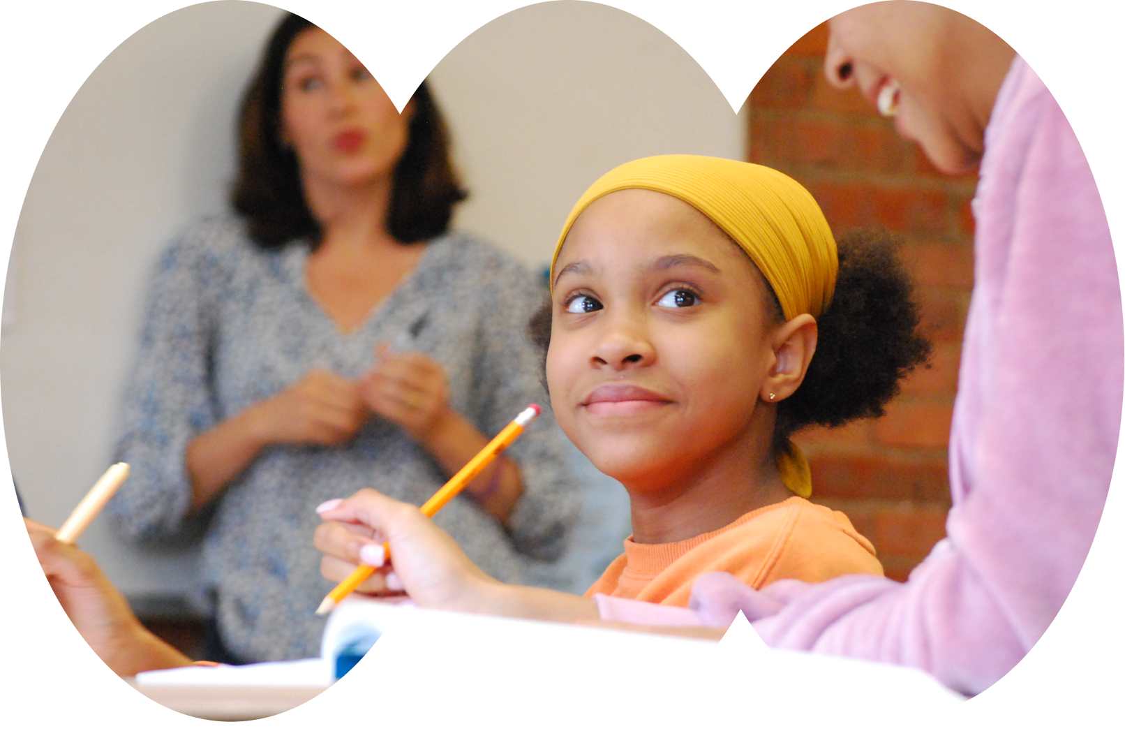 A student smiles in a classroom, sitting at her desk and holding a pencil while the teacher lectures in the background. The photo pops out of a fun, curvy modern cut out shape.