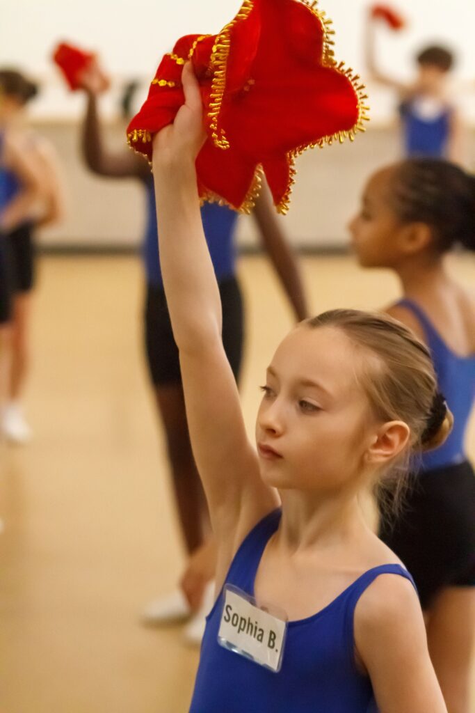 A close up of a young girl in a dance studio, dancing in a Chinese Folk Dancing class, holding a red handkerchief.