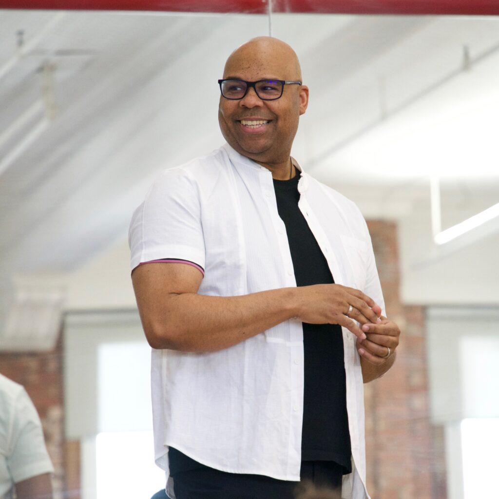 James Monroe Iglehart stands in front of a dance studio mirror, smiling.